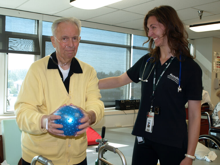 Female therapist standing with male patient holding blue ball