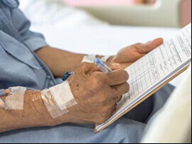 Close up of elderly person's hand signing a paper with IV taped to wrist.