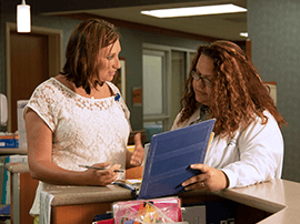 Two female nurses reviewing paperwork at nurse's station.
