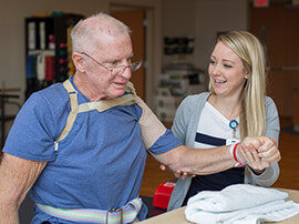 Young female therapist helping senior male patient do arm exercises.