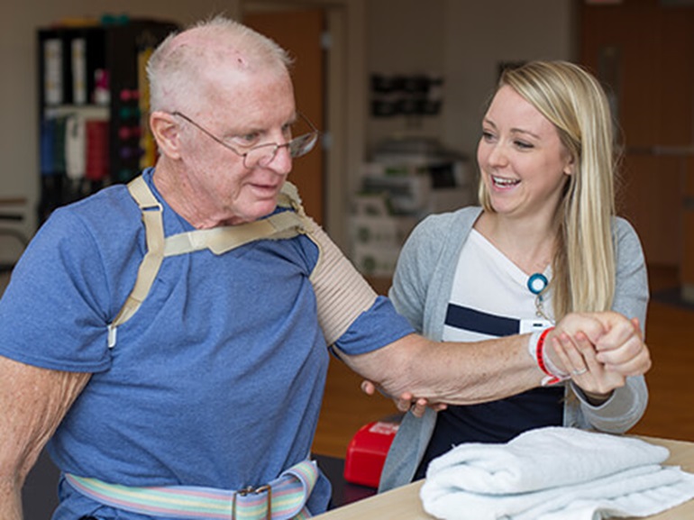 Young female therapist helping senior male patient do are exercises.
