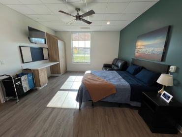 A patient room with a bed, tv, window and desk.