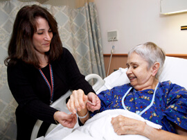 Female nurse putting wrist band on older female patient lying in bed.