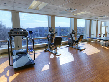 Gym equipment in front of large bank of windows.
