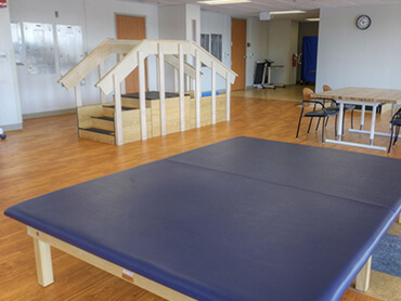 Wide angle view of therapy gym with large therapy table in front.