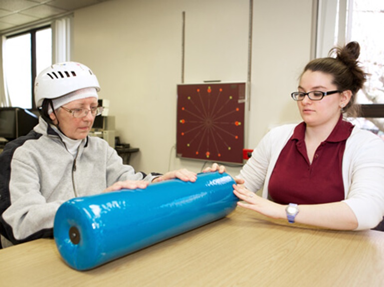 Female patient wearing a safety helmet witha large blue foam roller on a table.