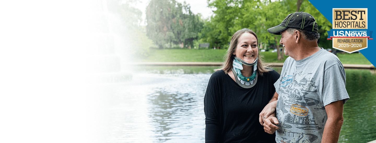 Two people standing together beside a reflecting pool in a park, with trees in the background and a “U.S. News Best Hospitals Rehabilitation 2025–2026” badge in the corner.