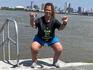 Kim doing a squat outside in front of a river with skyline behind her.