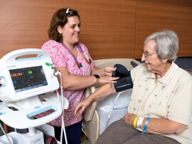 Nurse putting blood pressure cuff on female patient sitting in bed.