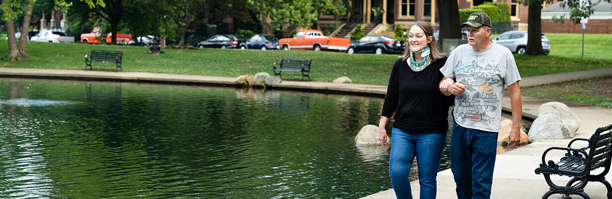 Woman wearing neck brace walks arm in arm with a man next to a pond.