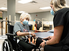 Nurse helps female patient in wheelchair adjust leg brace straps.