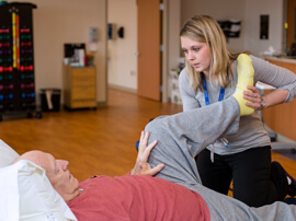 Female therapist holding foot of male patient lying on therapy table.
