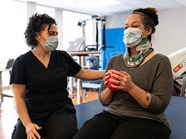 Female patient sitting on a therapy table and holding a small red ball.