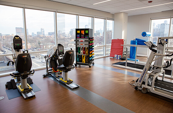 Photo of an indoor therapy gym with bikes, free weights, bands, treadmills and balance beams