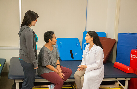 Two women are sitting at a table while another woman standing beside them speaking to each other
