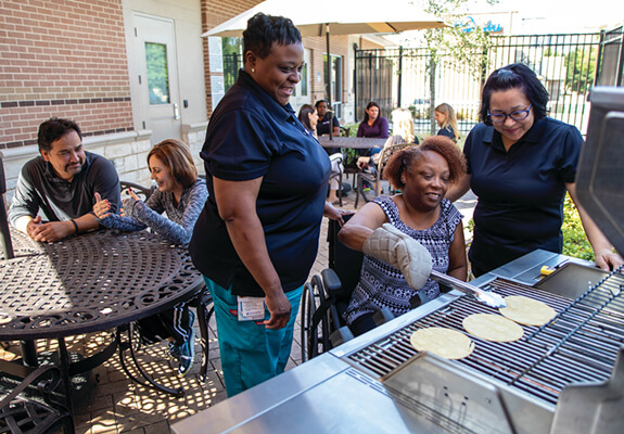 A patient and two staff members beside her while she is practicing grilling